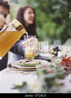 Un gruppo di persone in un giardino una celebrazione pasto con le impostazioni della tabella e frondosa decorazioni una persona mescita di bevande in bicchieri Foto Stock