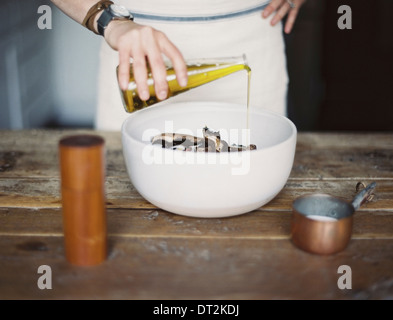 Una cucina domestica di una donna che indossa un grembiule medicazione una fresca insalata di verdure in una ciotola con olio Foto Stock