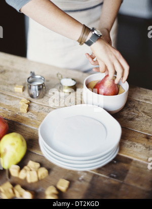 Una donna in una cucina domestica cucina fresca di immersione pere biologiche in una salsa per dessert freschi ingredienti marrone cubetti di zucchero Foto Stock