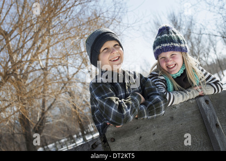 Paesaggio invernale con neve sul terreno due bambini in maglia cappelli appoggiato su di una recinzione Foto Stock