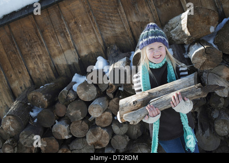 Paesaggio invernale con neve sul terreno una ragazza la raccolta di legna da ardere dalla pila di registro Foto Stock