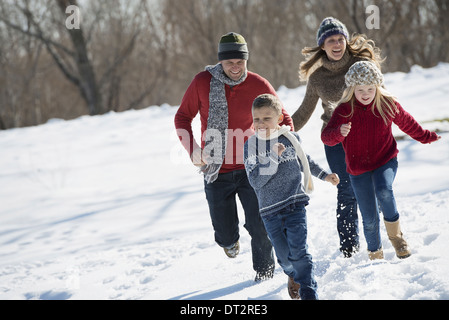 Paesaggio invernale con neve sul terreno famiglia a piedi due adulti a caccia di due bambini Foto Stock