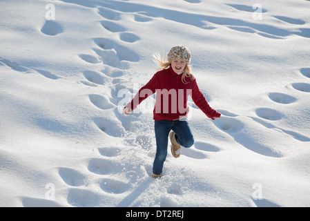 Paesaggio invernale con neve sul terreno di una giovane ragazza che corre attraverso la neve profonda rendendo le tracce di impronta Foto Stock