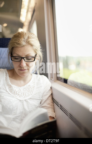 Una donna seduta da una finestra del treno la lettura di un libro Foto Stock