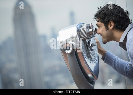 Vista sulla città giovane uomo cerca attraverso un telescopio sulla città Foto Stock