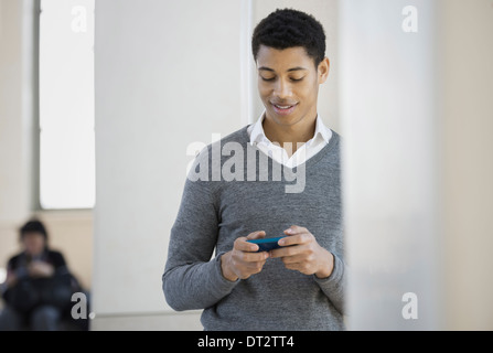 Un giovane uomo in un maglione grigio utilizzando il suo telefono cellulare Foto Stock