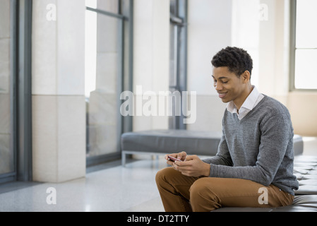 Uno stile di vita urbano un giovane uomo seduto in una lobby su un sedile unico con il suo telefono cellulare Foto Stock