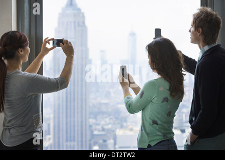 Uno stile di vita urbano tre persone in piedi su una piattaforma di osservazione utilizzando i loro telefoni cellulari per acquisire le immagini della vista sulla città Foto Stock