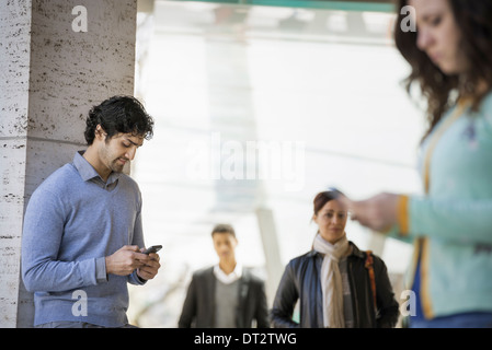 Tre persone sul marciapiede di un uomo e di una donna giovane utilizzando i loro telefoni cellulari e due persone a camminare sul marciapiede Foto Stock
