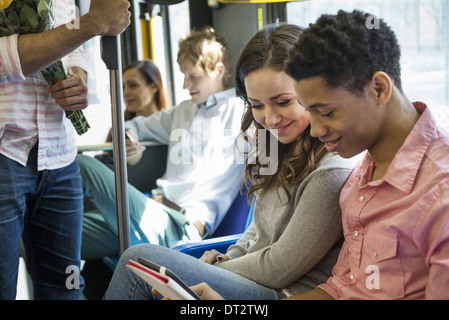 Uno stile di vita urbano di un gruppo di persone che gli uomini e le donne su un autobus cittadino di New York City un paio di fianco a fianco guardando una tavoletta digitale Foto Stock