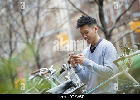 Vista su cityA uomo in un maglione blu da una fila di biciclette parcheggiate il controllo dei suoi messaggi su un telefono intelligente Foto Stock