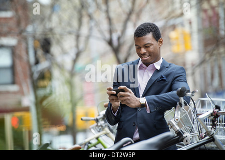 Vista su cityA giovane uomo in una tuta blu da un parcheggio biciclette controllando il suo smart phone per i messaggi Foto Stock