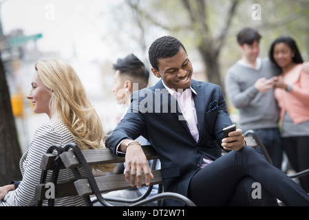 Vista sulla città si radunò intorno a una panchina nel parco due controllando uno smart phone per i messaggi Foto Stock