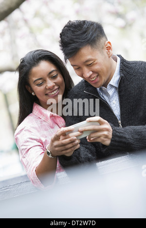 Vista su cityYoung persone all'aperto in un parco cittadino un paio di fianco a fianco che guarda uno smart phone Foto Stock