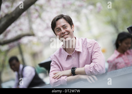 Vista su cityA uomo seduto all'esterno in un parco della città guardando la telecamera e sorridente Foto Stock
