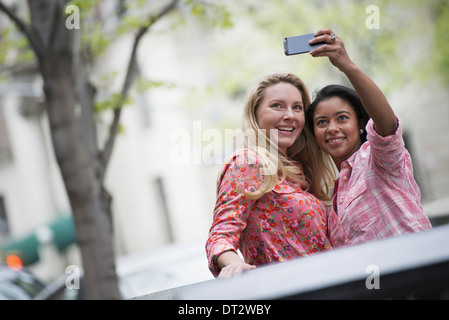 Vista su cityYoung persone all'aperto in un parco cittadino di due donne che prendono un autoritratto o selfy con uno smart phone Foto Stock