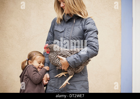 Donna che mantiene un bianco e nero il pollo con un rosso coxcomb sotto un braccio di una giovane ragazza accanto a lei mentre tiene il suo altro lato Foto Stock