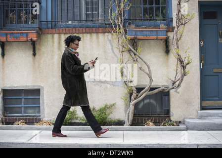 Una donna in un caldo cappotto camminando lungo la strada per controllare il suo telefono Foto Stock