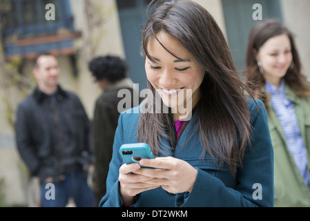 Una donna controllando il suo turchese smart phone tra altre persone su una strada di città Foto Stock