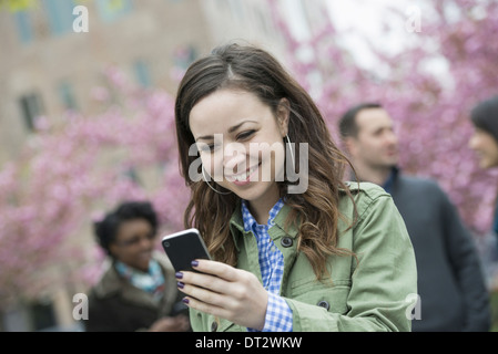 Una giovane donna controllando il suo smart phone per i messaggi nel parco un gruppo di amici in background Foto Stock