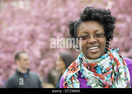 Un gruppo di persone di fiori di ciliegio gli alberi del parco una giovane donna sorridente e guardando la telecamera che indossa una sciarpa floreale Foto Stock