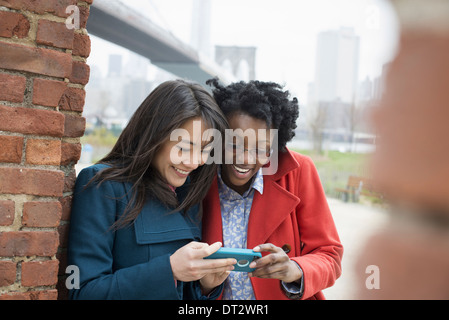 Ponte di Brooklyn attraversando la East River due donne affiancate controllo dello schermo di un telefono intelligente e ridere Foto Stock