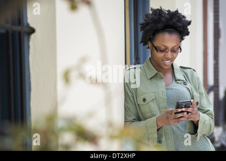 Una donna appoggiata contro un infisso controllando il suo telefono Foto Stock