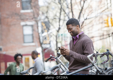 Un giovane uomo di controllare il suo telefono e ciclo texting rack e memorizzate le biciclette Foto Stock