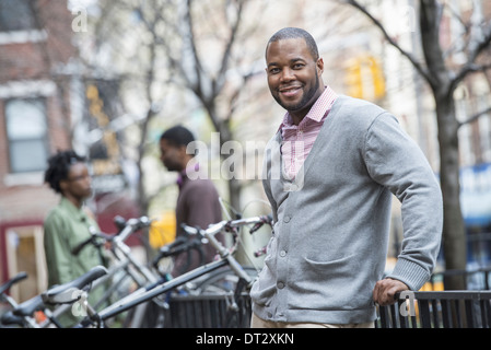 Un uomo che utilizza il proprio telefono in un gruppo di persone in background rack di ciclo Foto Stock