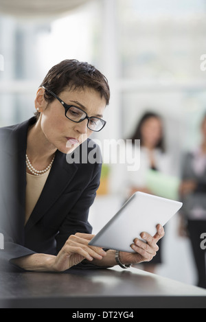 Un ufficio interno di una donna in una giacca nera con una tavoletta digitale Foto Stock