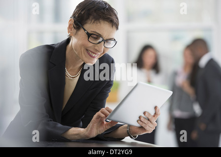 Un ufficio interno di una donna in una giacca nera con una tavoletta digitale Foto Stock