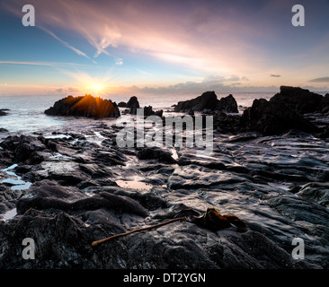 Ocean sunrise su una spiaggia rocciosa a Looe in sud Cornovaglia Foto Stock