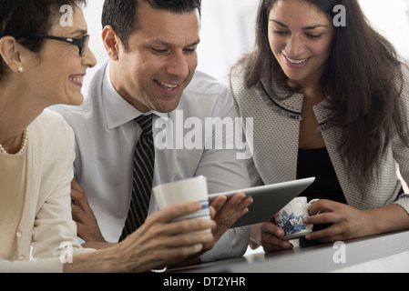 I giovani professionisti al lavoro tre colleghi due uomini e una donna guardando lo schermo di una tavoletta digitale Foto Stock