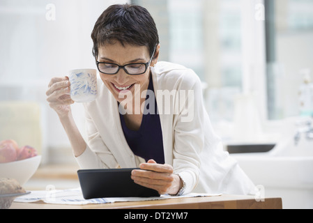 La città di New York una donna vestita per lavorare in camicia crema tenendo una tazza di caffè controllando la sua tavoletta digitale Foto Stock