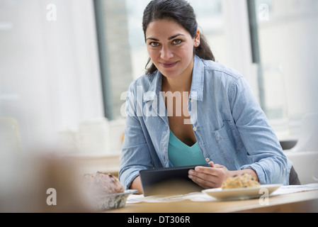 In un ufficio o un interno dell appartamento a New York City una giovane donna in un denim shirt utilizzando una tavoletta digitale Foto Stock