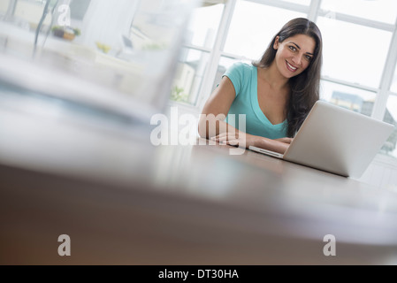 Una giovane donna comodamente seduto in una tranquilla arioso ambiente office utilizzando un computer portatile Foto Stock