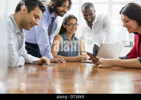 La gente di affari si sono riuniti in un ufficio nella città di un team di cinque persone uomini e donne raccogliendo attorno a un computer portatile Foto Stock