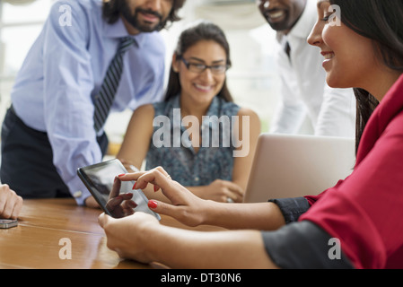 La gente di affari si sono riuniti in un ufficio nella città di un team di quattro persone uomini e donne raccogliendo attorno a un computer portatile Foto Stock