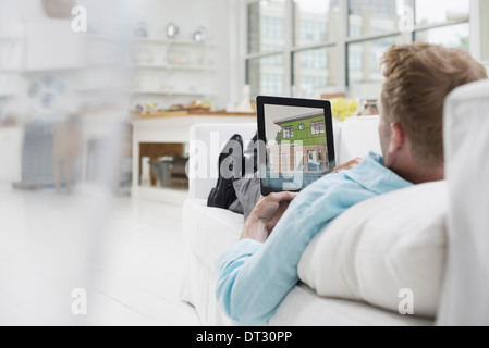 Un uomo disteso su un divano nel comfort di una tranquilla arioso ambiente office utilizzando una tavoletta digitale Foto Stock