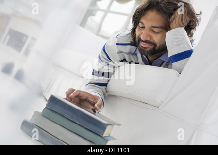 Uomo disteso sul suo stomaco su un divano in una tranquilla arioso ambiente office utilizzando un telefono intelligente Foto Stock