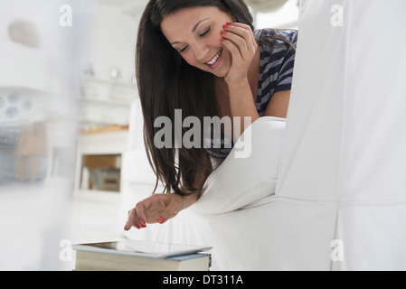 La gente di affari ufficio estate una donna sdraiata sulla sua parte anteriore su un divano in un tranquillo arioso ambiente office utilizzando un telefono intelligente Foto Stock