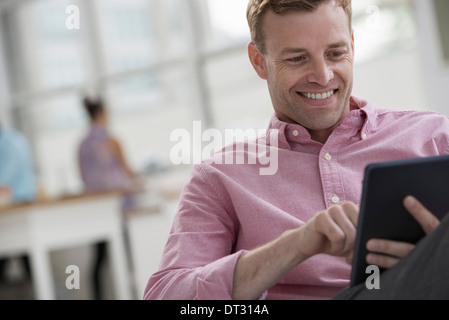 Un Uomo in camicia rosa seduta sorridente utilizzando una tavoletta digitale Foto Stock