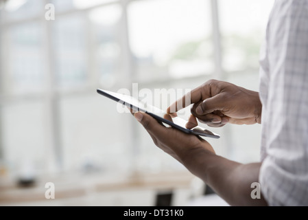 Professionisti in ufficio una luminosa e ariosa e posto di lavoro di un Uomo in camicia bianca utilizzando una tavoletta digitale Foto Stock