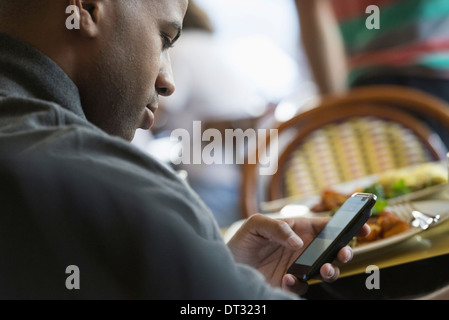 Un uomo seduto in un bar controllando il suo smart phone Foto Stock