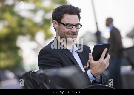 Un uomo seduto su una panchina utilizzando una tavoletta digitale Foto Stock