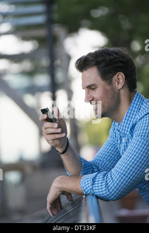 Un Uomo in camicia blu utilizzando una smart phone Foto Stock