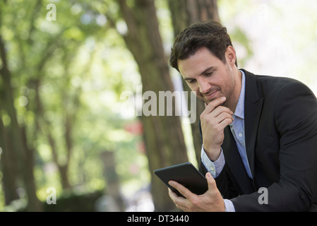 Un uomo seduto in un parco con la sua tavoletta digitale Foto Stock