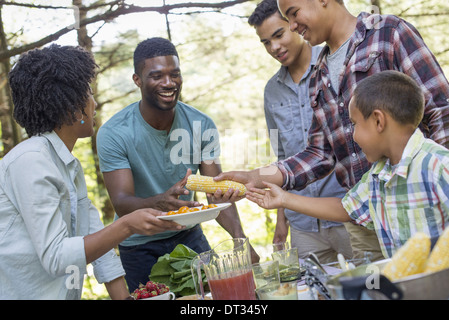 Un picnic in famiglia in un ombroso bosco di adulti e bambini intorno a un tavolo consegna intorno a piastre e cibo Foto Stock