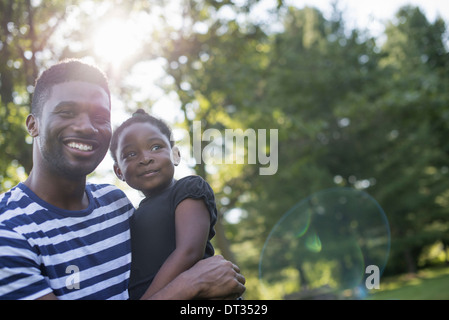 Un uomo con un bambino nelle braccia all'ombra di alberi in una calda giornata estiva Foto Stock