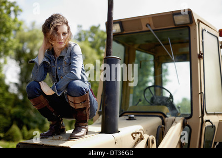 Una giovane donna in denim camicia e stivali su il cofano di un trattore Foto Stock